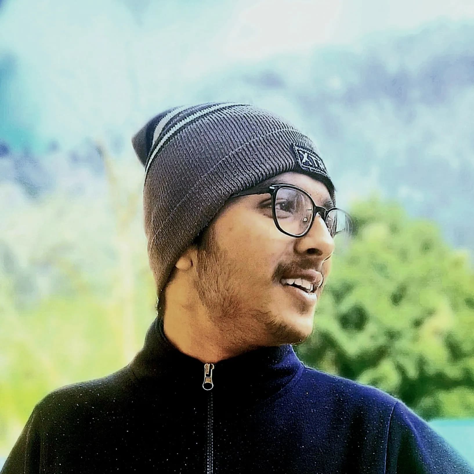 Gantavya in a beanie, laughing, with hills behind